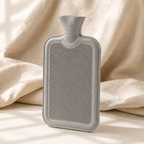 Bouillotte à eau gris clair présentée debout sur du linge de lit