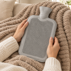 Mains tenant une bouillotte à eau gris clair sur un plaid beige