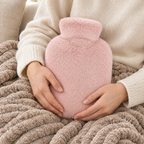 Mains posées sur la housse de bouillotte rose poudré, sur un plaid en maille