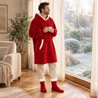 Homme en sweat plaid rouge et chaussettes pilou-pilou rouges devant la fenêtre, un café à la main